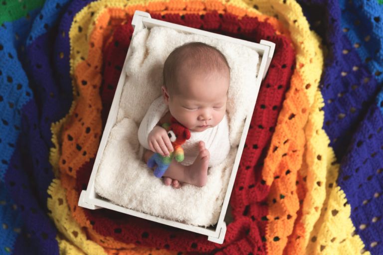 newborn baby surrounded by rainbow blanket
