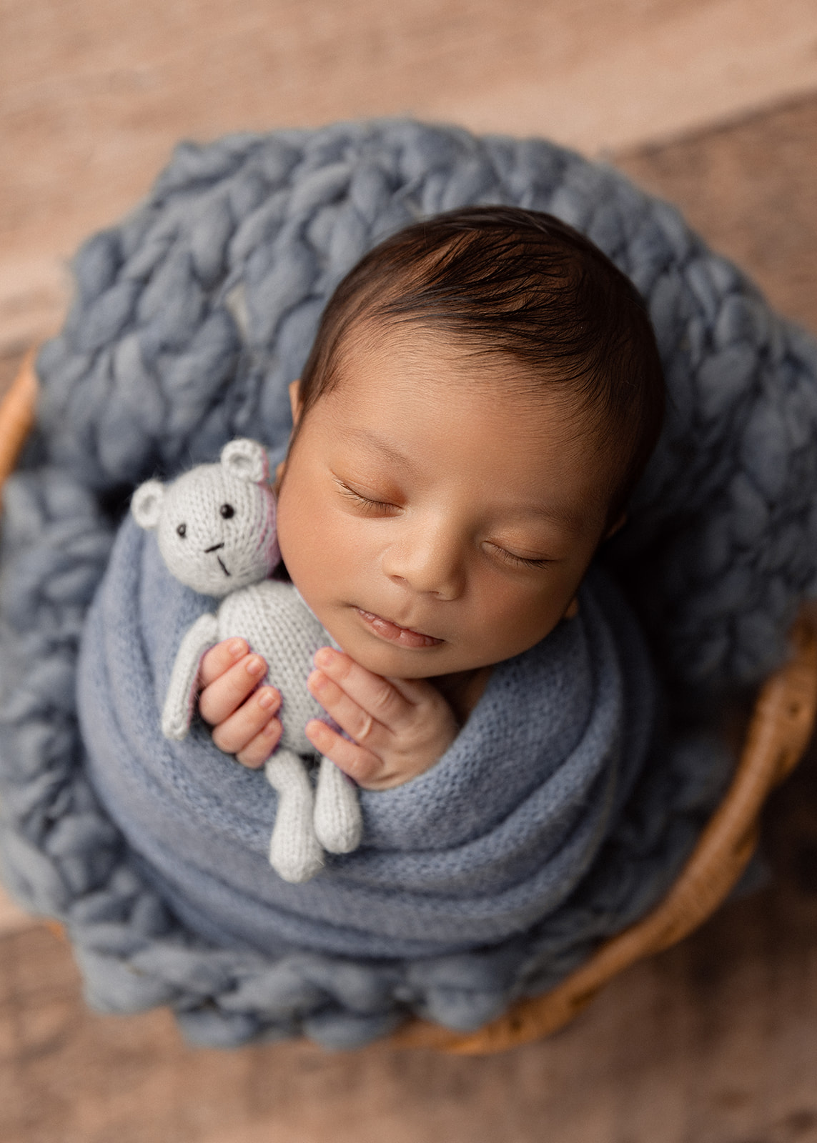 a baby boy in a basket sleeping and grasping a teddy