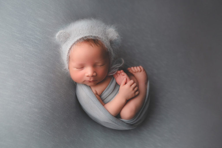 sleeping newborn boy wearing a teddy bear bonnet