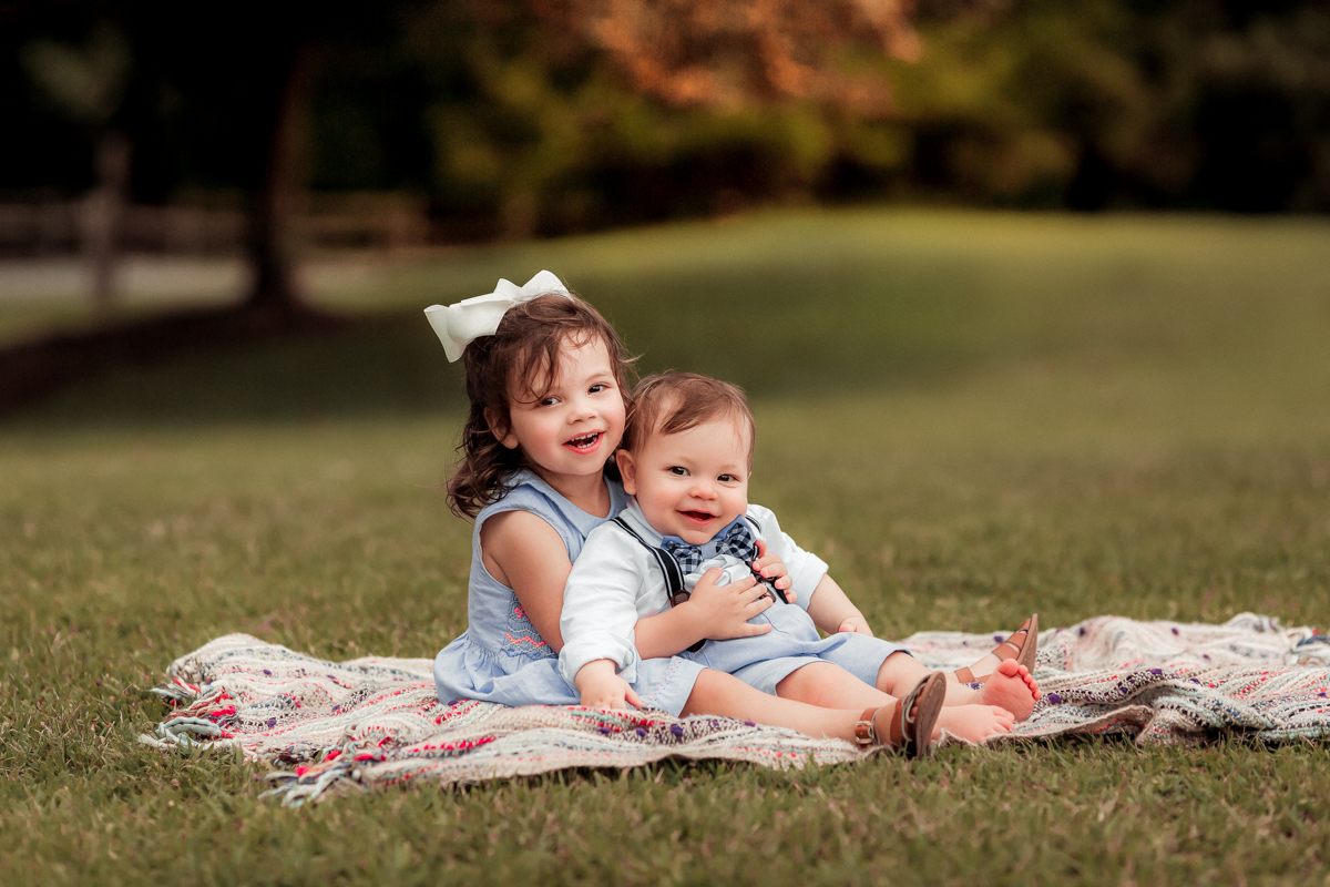 a toddler girl holding her baby brother in her lap while they smile