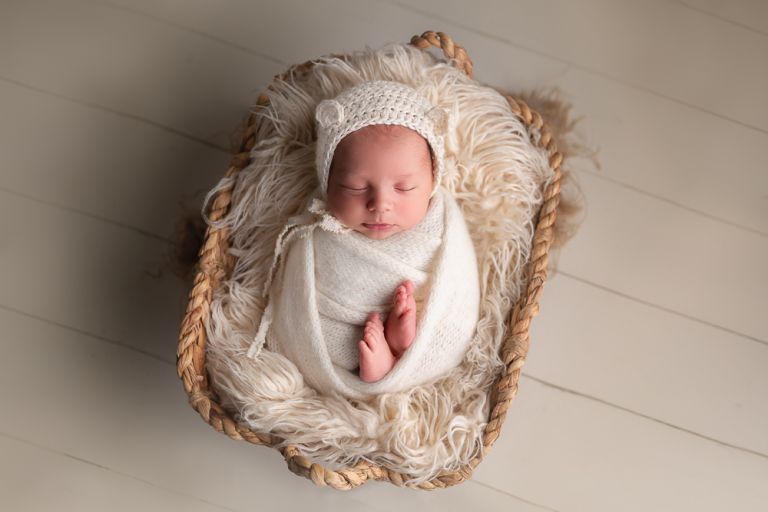 newborn baby wrapped in white in a basket