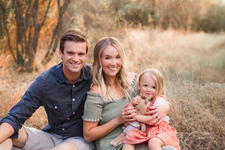 Mom, dad, and little girl snuggled on a blanket for a photo