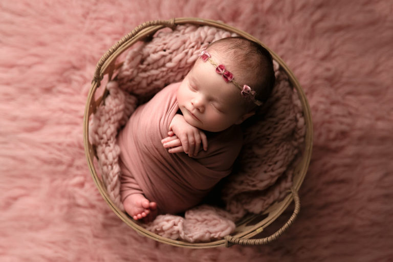 newborn baby girl wrapped in pink sleeping in a basket