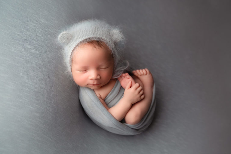 sleeping newborn baby boy wearing a teddy bear bonnet