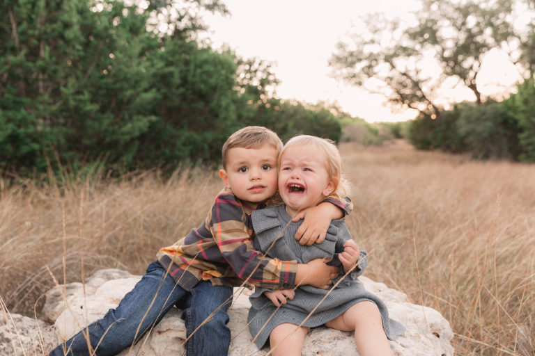 Crying toddler with her uncertain big brother hugging her