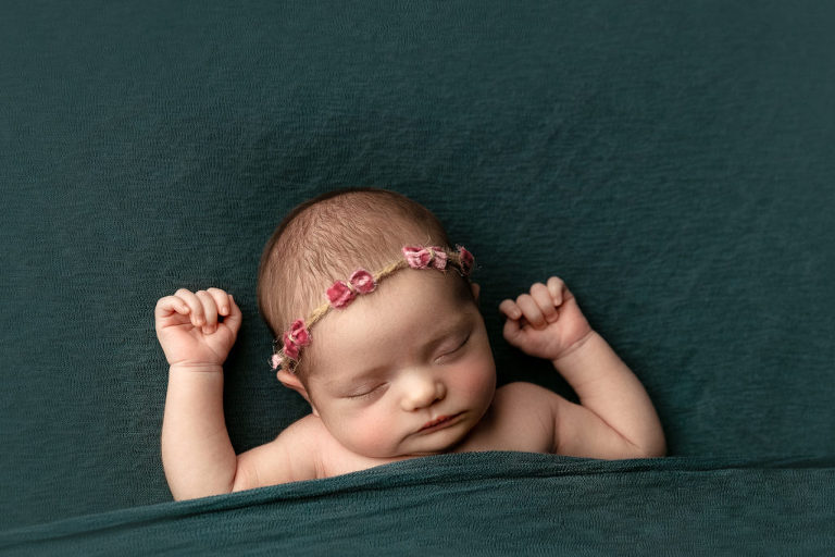 Baby girl with a headband sleeping on her back on teal blanket