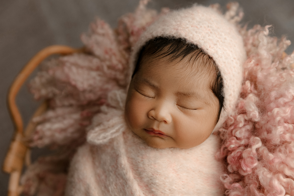 newborn baby girl with pink bonnet sleeping in pink basket