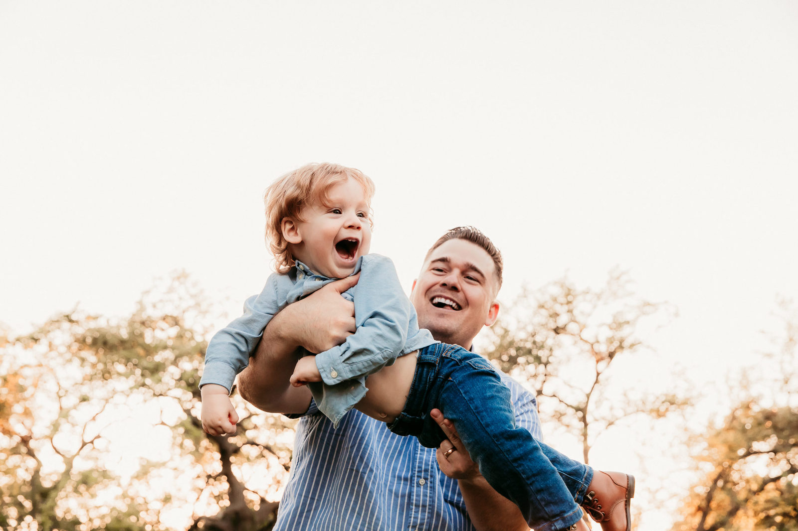 dad swinging his toddler son in the air while the child laughs